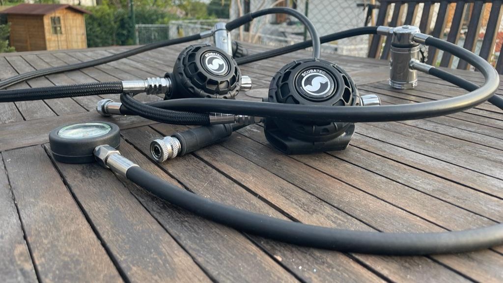 Vista ravvicinata di un erogatore subacqueo e manometro posizionati su un tavolo di legno.