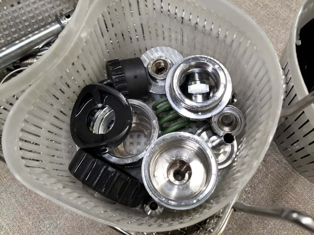 Parti metalliche di un erogatore subacqueo all'interno di un cestino, pronte per la manutenzione e revisione.